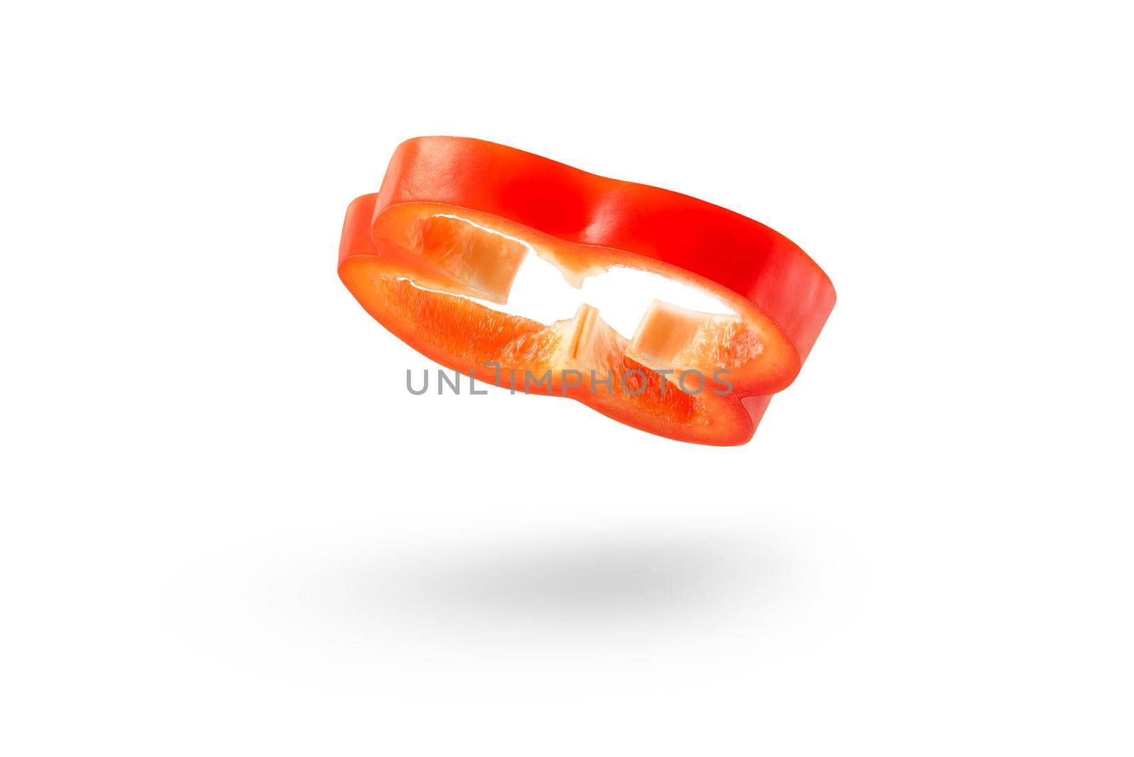 A slice of red paprika falls on a white backdrop. Red bell pepper flying in air on isolated white background.
