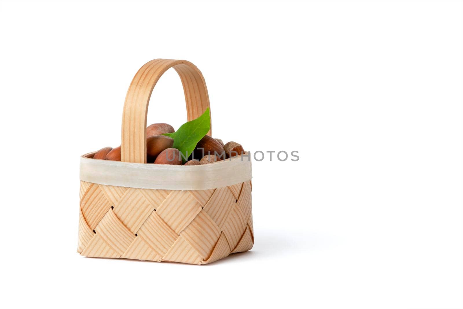 Hazelnut lies in a wooden basket on a white isolated background. Unpeeled hazelnuts in shell and green leaves.