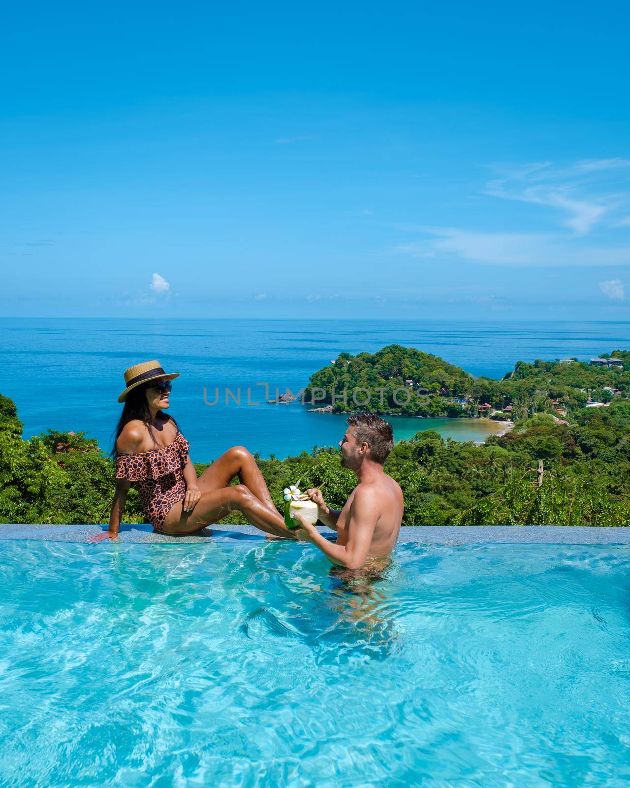 a young couple of men and women at a swimming pool during a vacation on a tropical island. man and woman in infinity pool during sunset. luxury vacation in Thailand pool of a luxury pool villa
