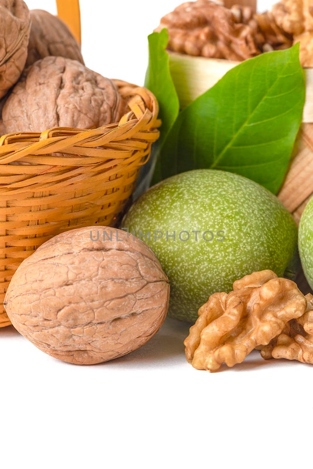 Walnut. Walnut fruits of different varieties lie in wooden saucers and baskets on a white isolated background. Nearby are green leaves and unripe walnut fruits