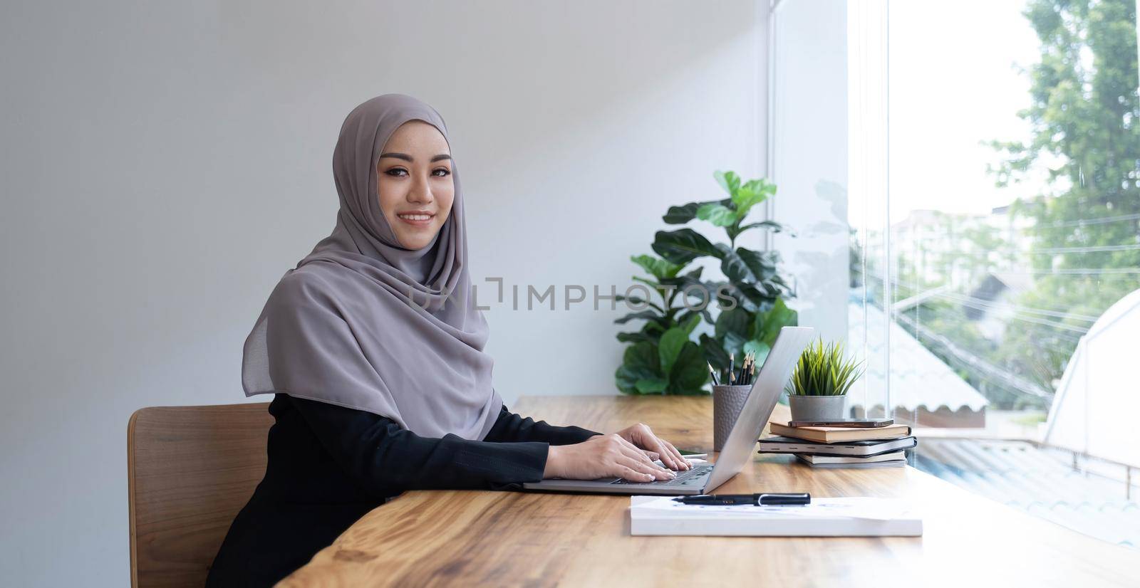 Happy arab woman freelancer chatting with clients on laptop, sitting at cafe, empty space by wichayada