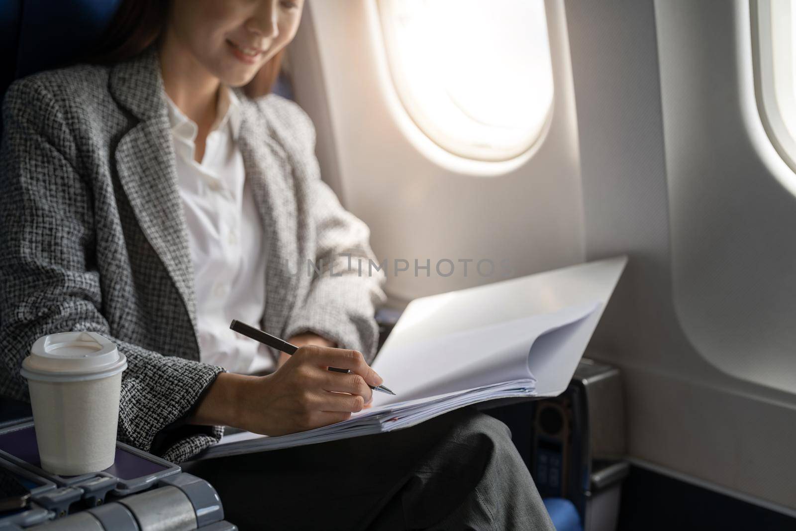 Close up hand of asian female entrepreneur working on paperwork finance report sitting near window in an airplane.