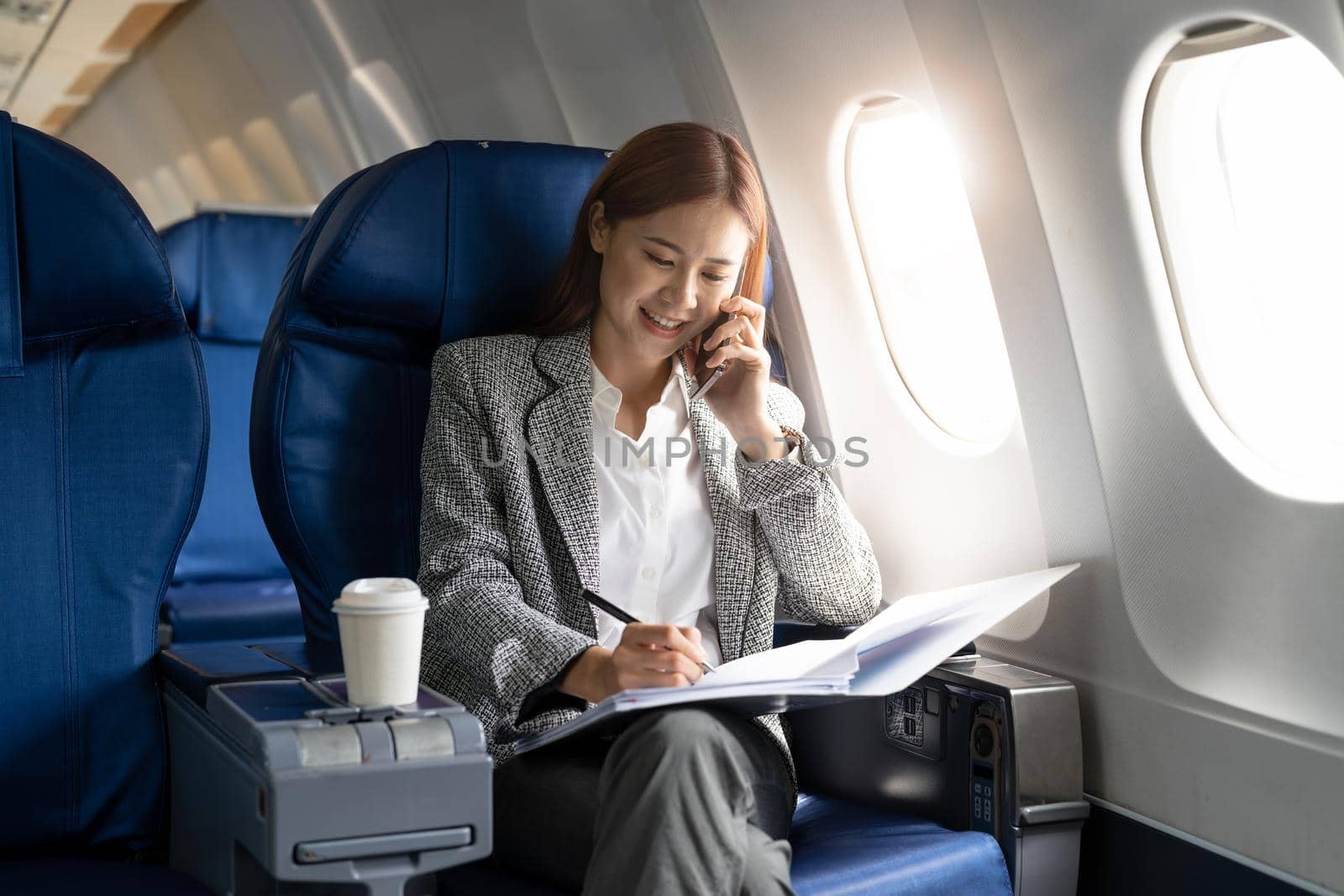 Business young asian woman talking on phone during working for paperwork financial report on airplane, flight in plane.