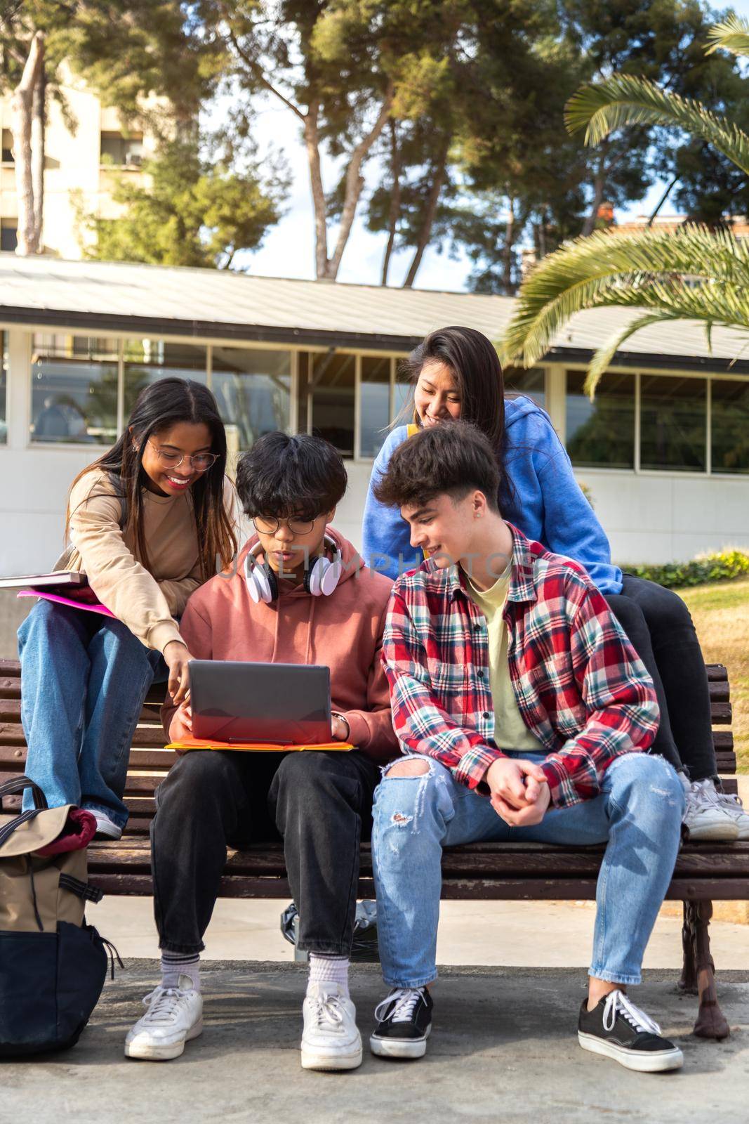 Multiracial college student doing university research homework and studying together on campus sitting on a bench. Young people using laptop. Vertical image. higher education and technology concept.