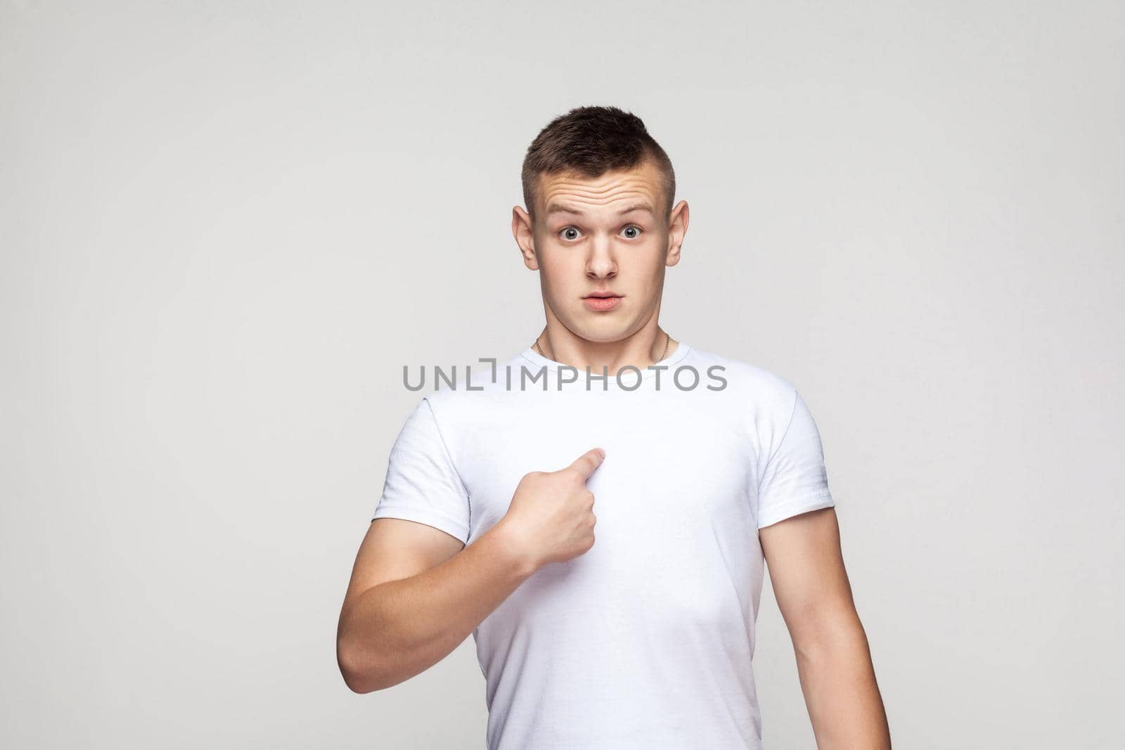 Surprised boy looking at camera and pointing finger himself. Studio shot