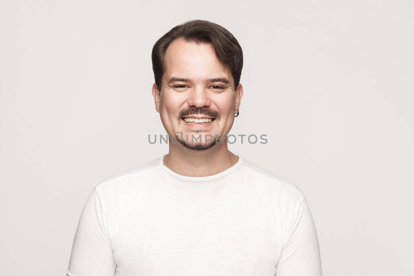 Happiness adult man, looking at camera and toothy smile. Indoor shot in gray background