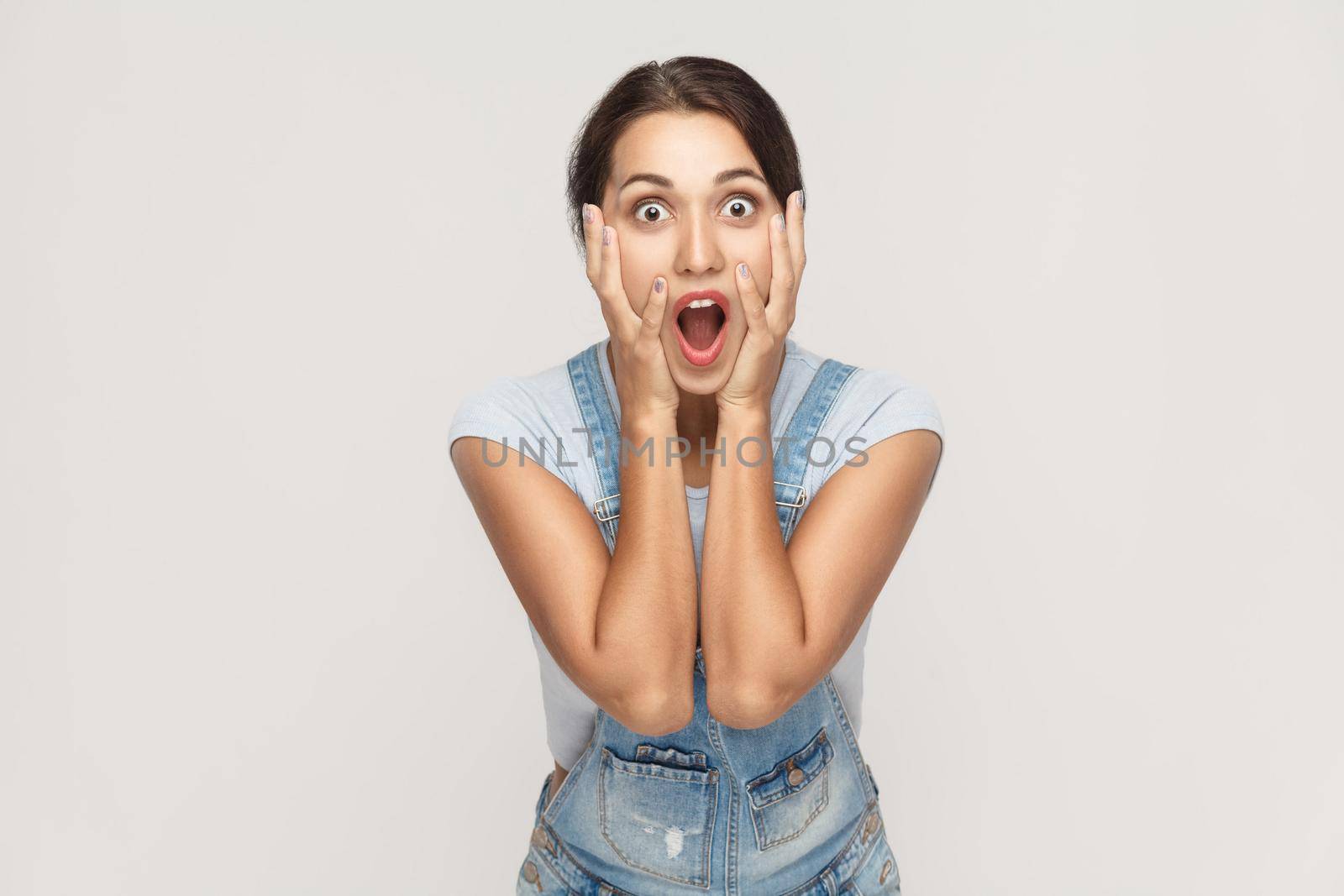 Human face expressions and emotions. Arab young adult woman holding arms on her cheeks and shocked. Isolated on gray background, studio shot