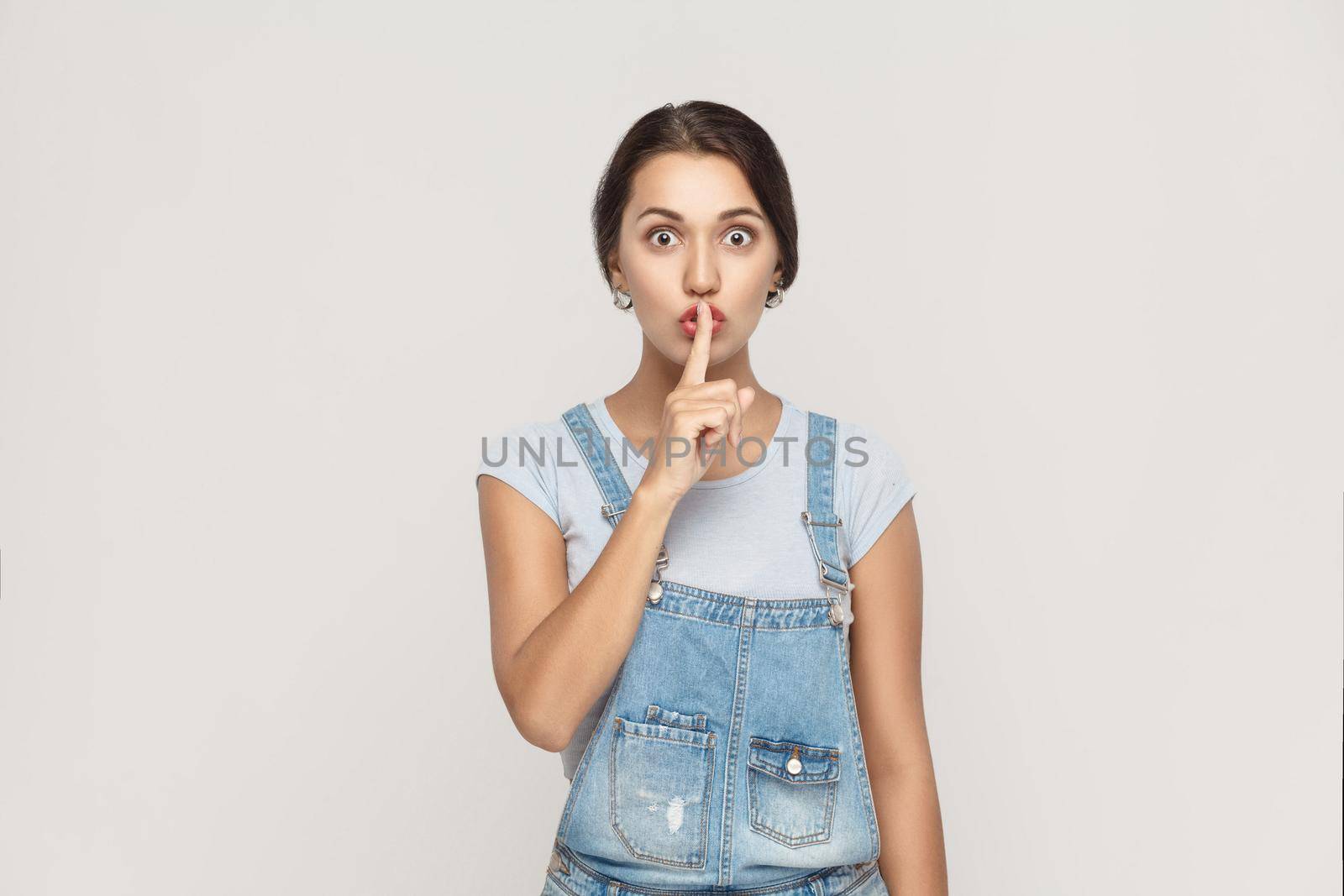 Shh sign. Beautiful indian woman looking at camera with silent sign. Studio shot, on gray background.