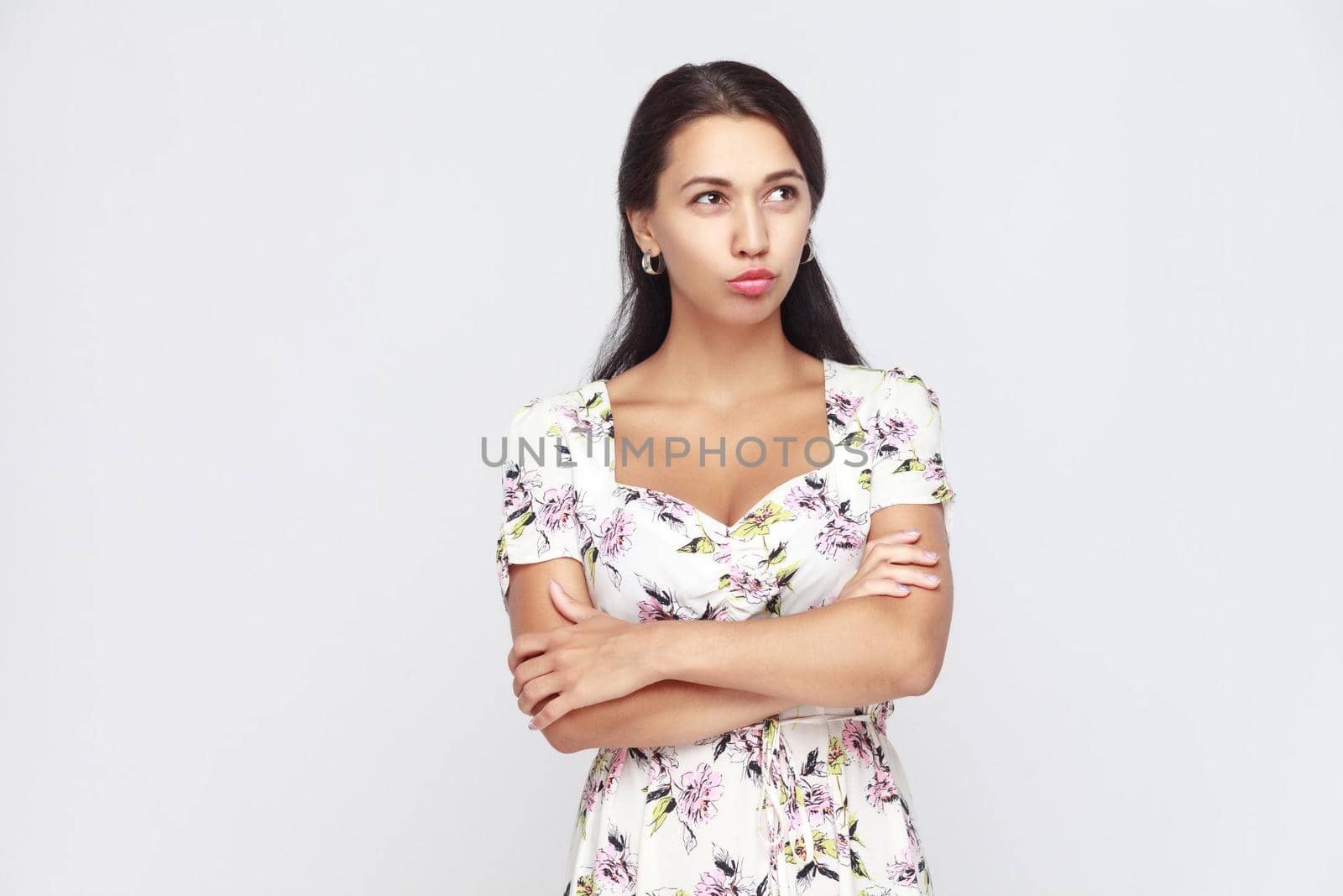 Beautiful woman crossed hands, looking up and thinking. Studio shot on gray background