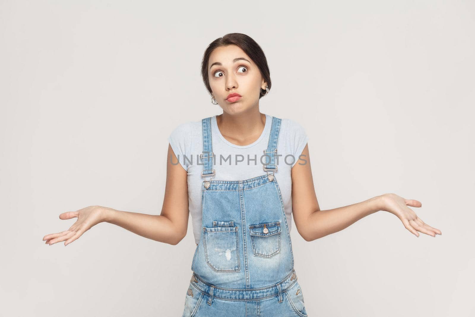 Negative human emotions, facial expressions. Puzzled young adult woman with arms out, shrugging her shoulders, saying: who cares, so what, I don't know. Isolated studio shot on gray background.