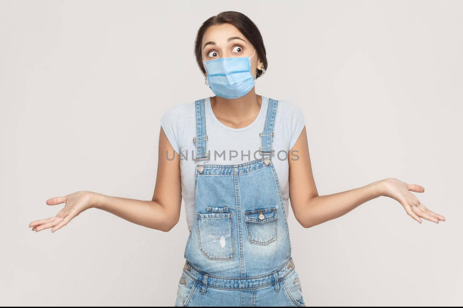 young woman with medical mask in denim overalls standing raised arms and looking away. by Khosro1