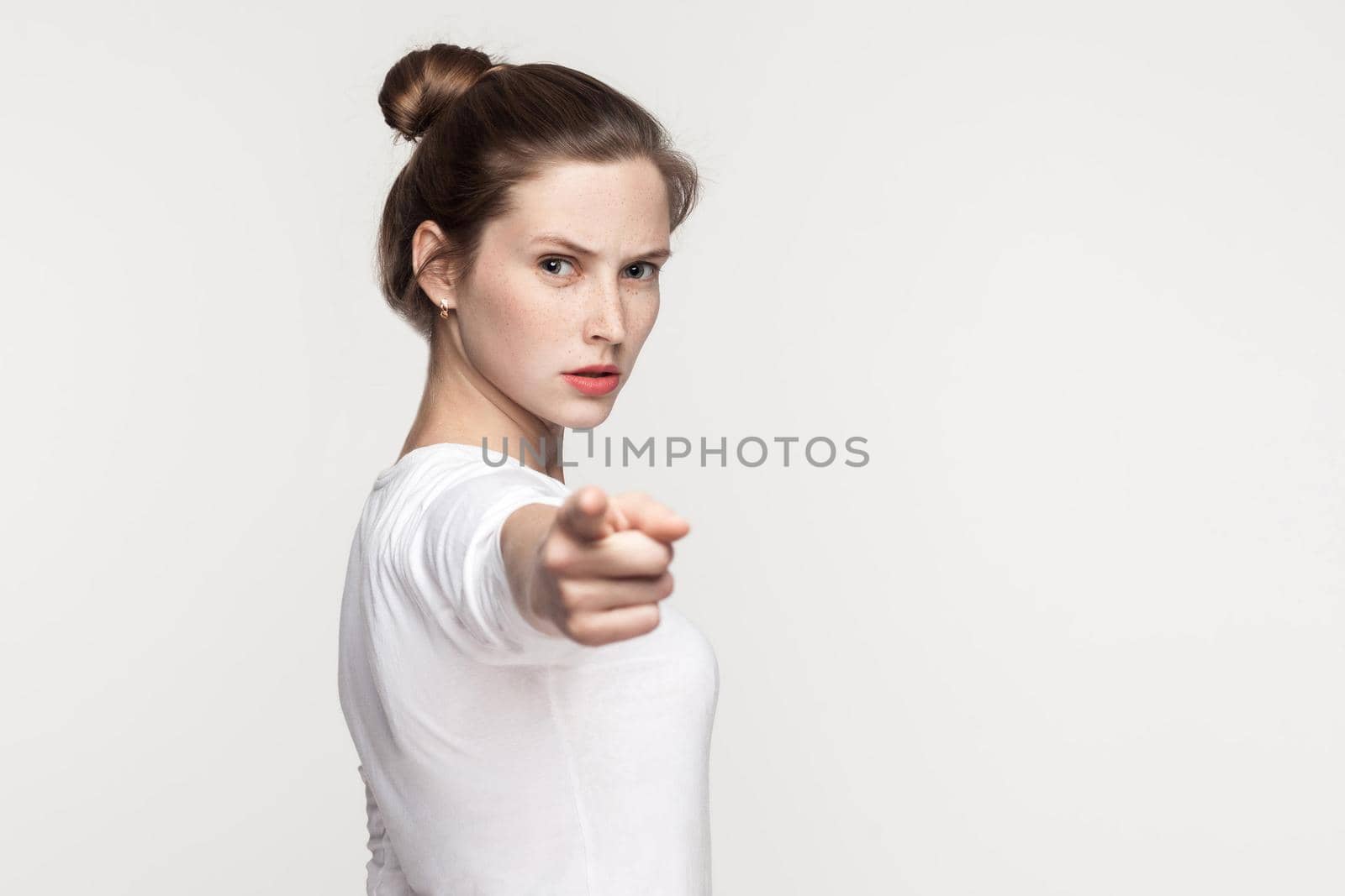 Hey you! Freckles woman pointing finger at camera. Studio shot