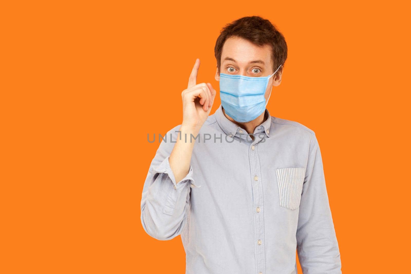 I have idea. Portrait of excited young worker man with surgical medical mask standing with surprised face and has a idea. indoor studio shot isolated on orange background.