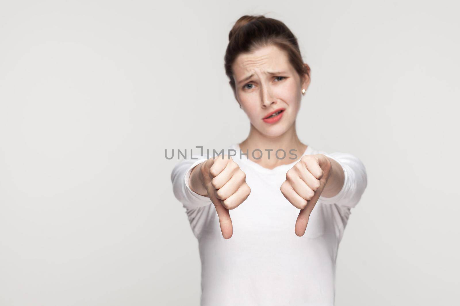 Unhappy woman demonstrate dislike sign. Studio shot, gray background