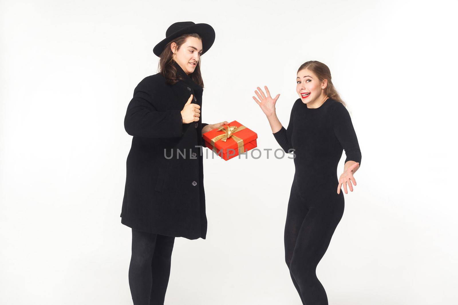 Man in coat and hat present gift box confused woman. Studio shot, isolated on white background