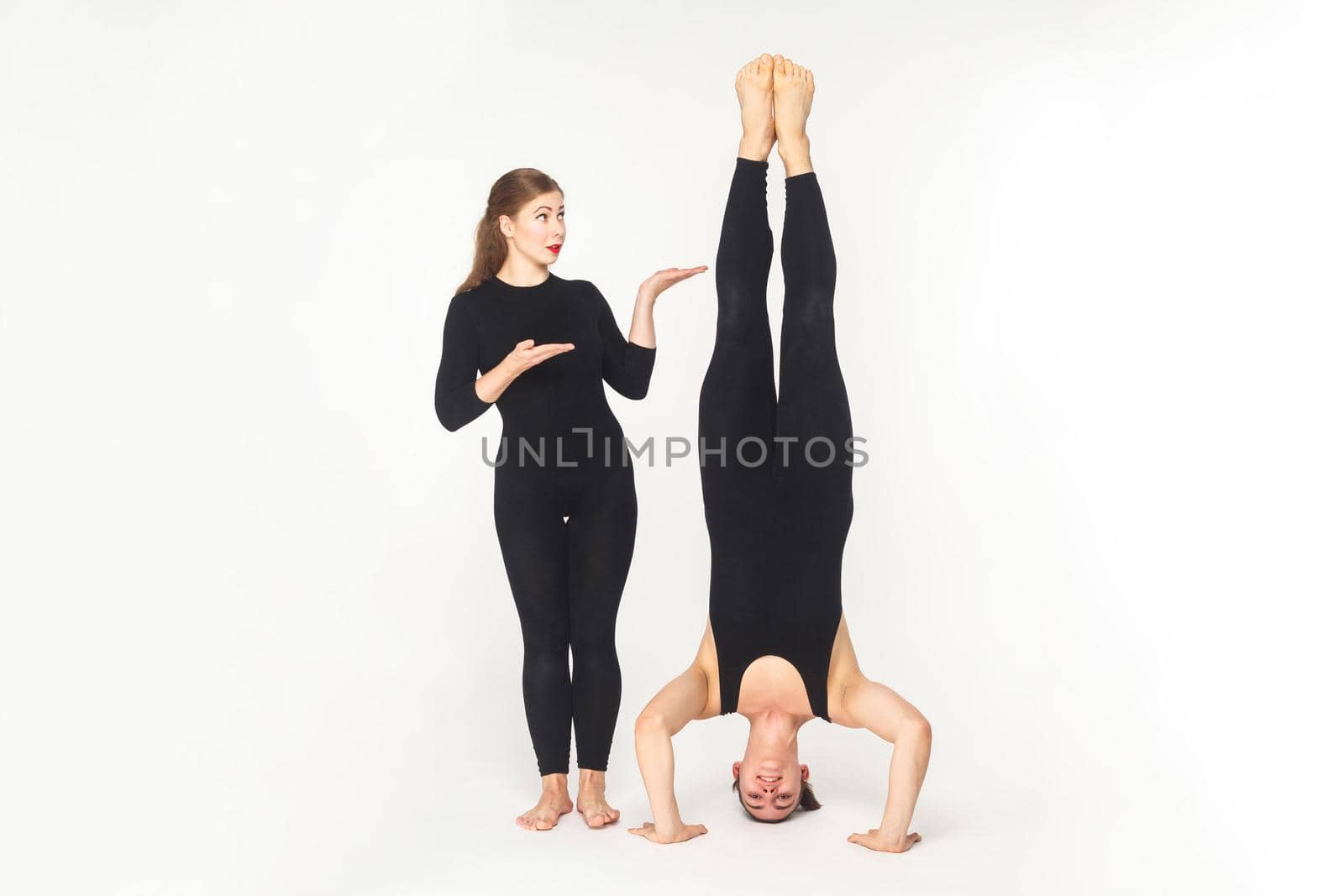 Vice versa. Woman showing at man, stand on head. Studio shot, isolated on white background