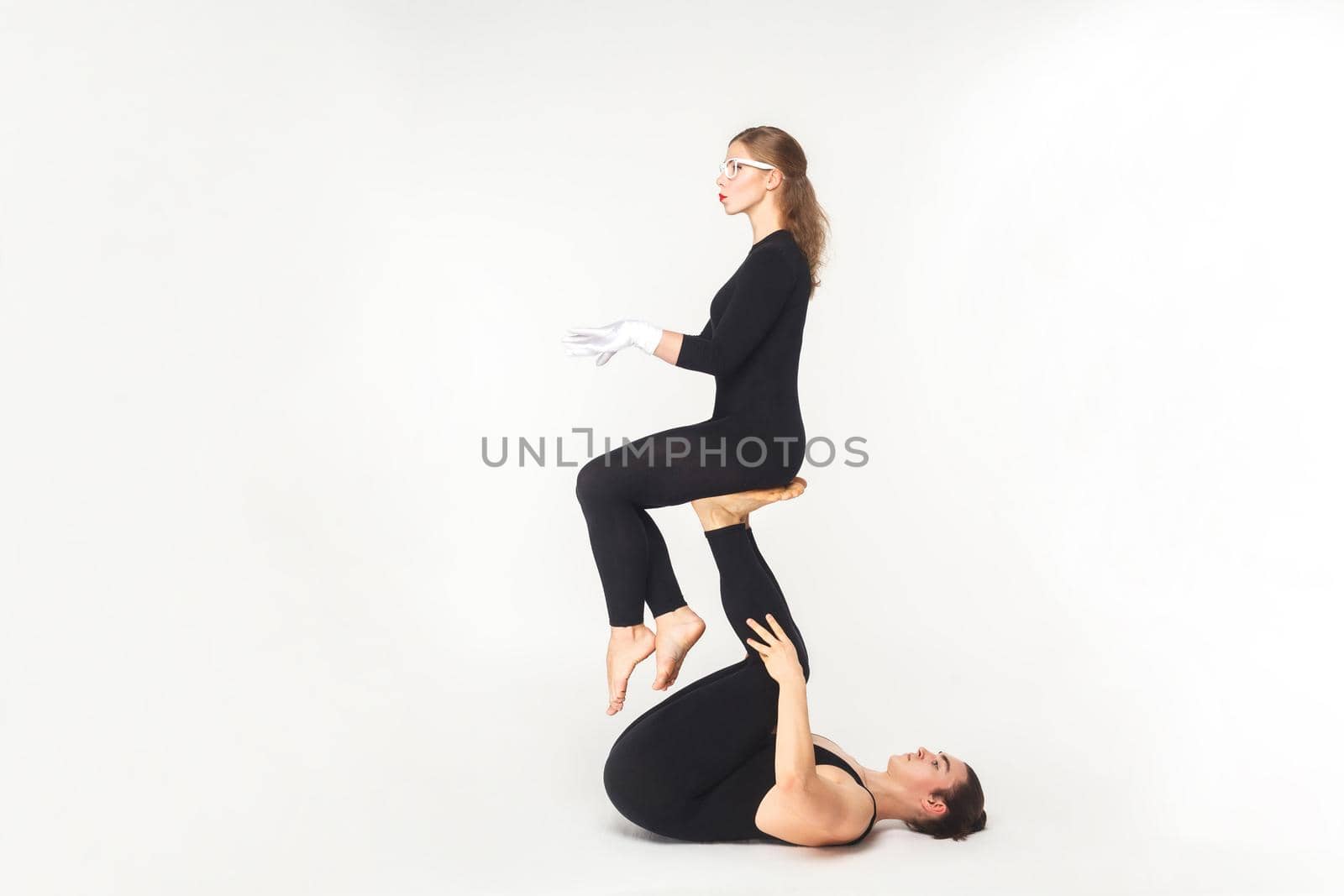Acrobatic concept, sit pose. Young man holding woman legs, balancing. Studio shot, isolated on white background
