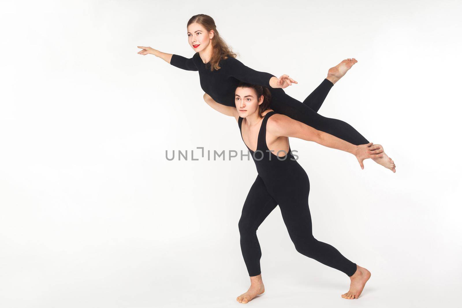 Acrobatic concept, fly pose. Young man holding woman and balancing. Studio shot, isolated on white background