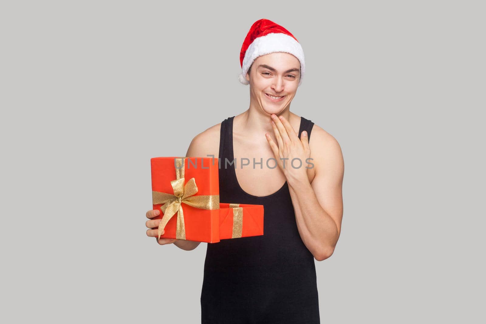 Cunning man holding gift box touching his chin and toothy smiling looking at camera with funny face. by Khosro1