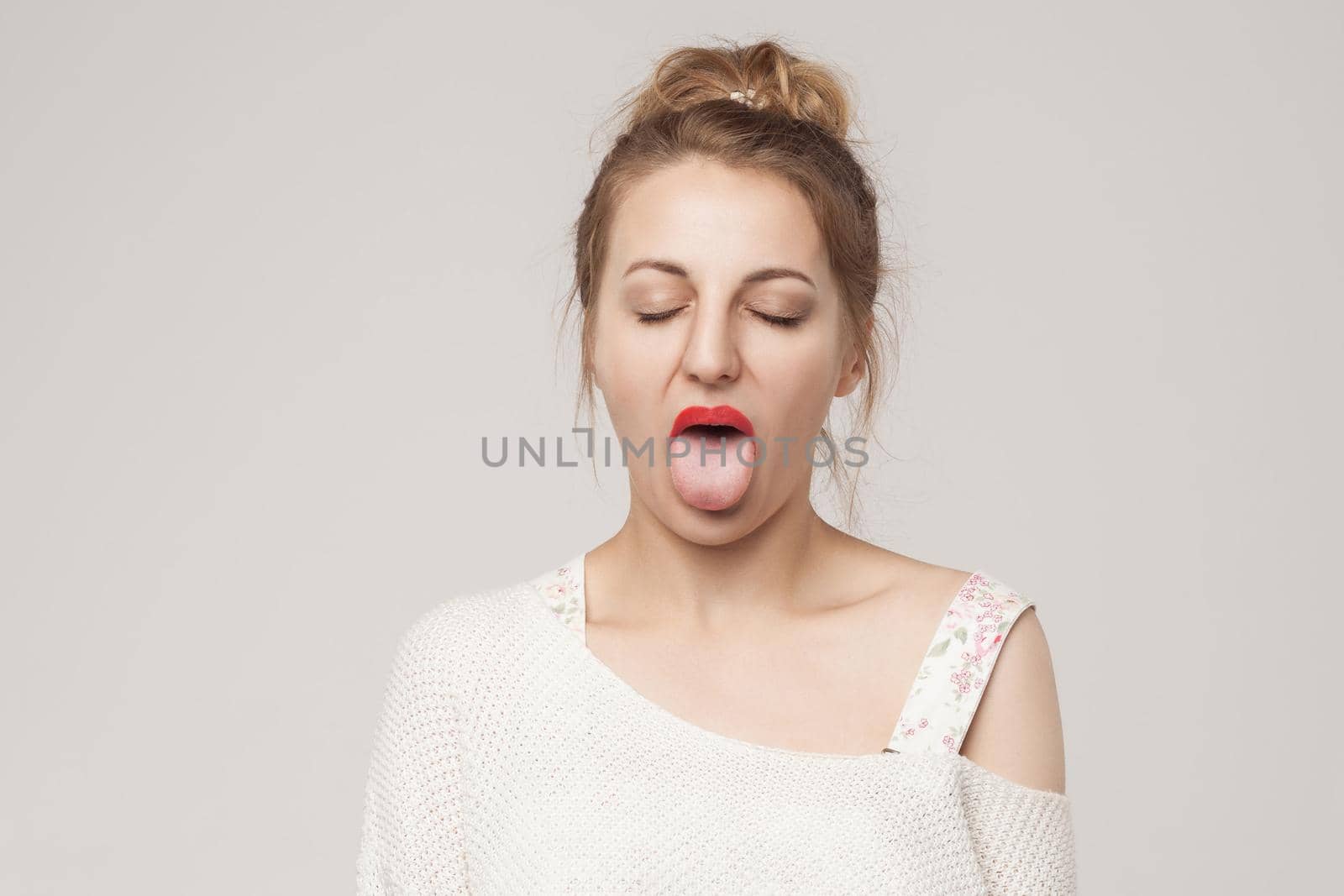 Funny woman closed eyes and tongue out . Studio shot, isolated on gray background