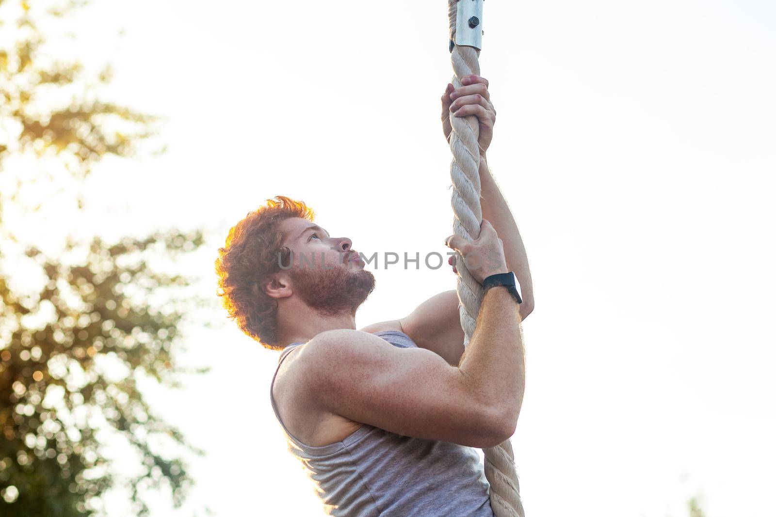 Climed higer and higher. Ginger sportsman doing exercise at rope. outdoor shot