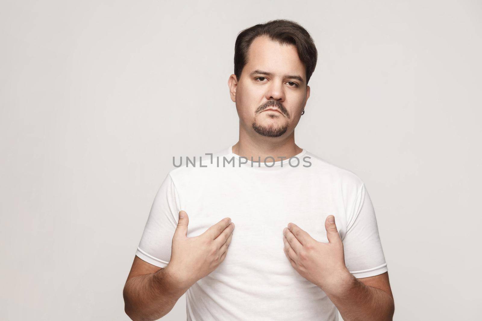 Arrogant and proud adult man pointing hands himself and looking at camera. Studio shot, gray wall