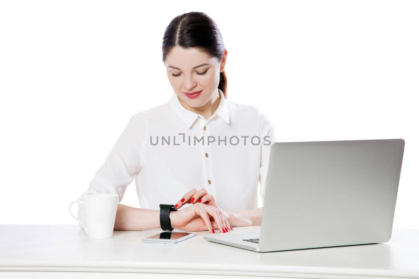 Portrait of happy attractive brunette businesswoman in white shirt sitting looking and touching her smartwatch display, reading something and smiling. indoor studio shot, isolated in white background.