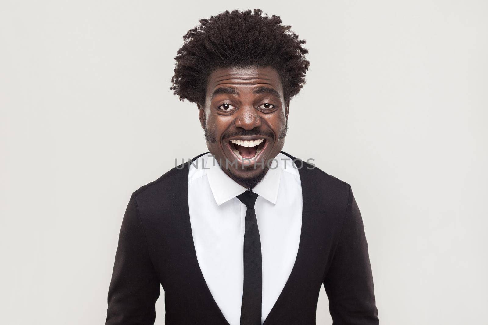 Laughing afro businessman looking at camera and toothy smiling. Studio shot, gray background