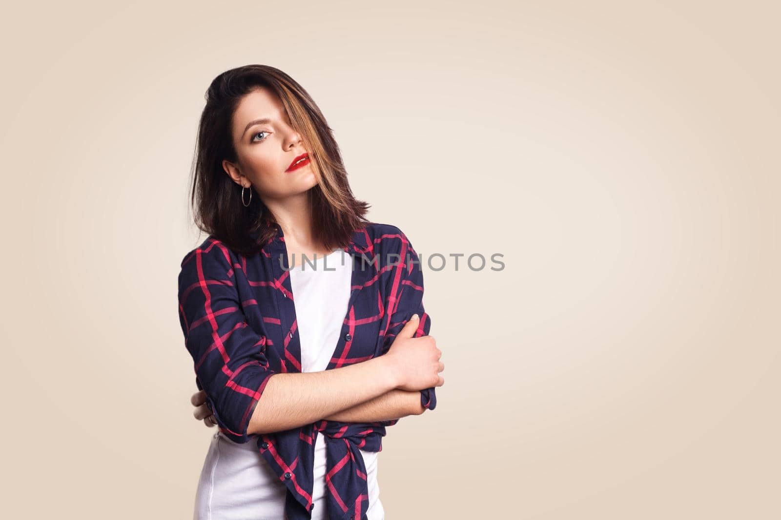 Portrait of beautiful happy girl in casual style with makeup and black bun hairstyle looking at camera with crossed arms. studio shot on beige background.