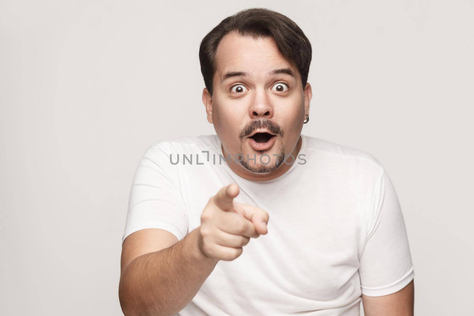 The adult man, opening mouths widely, having surprised shocked looks, pointing finger at camera. Isolated studio shot on gray background