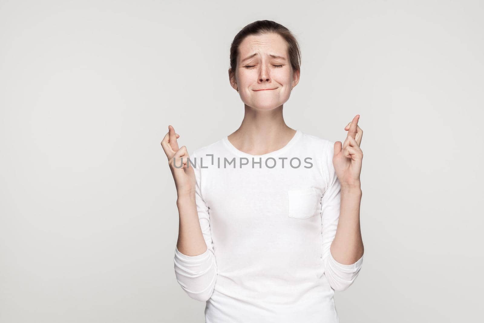 I wish some cool. Young beautiful girl closed eyes and crossed fingers. Studio shot,isolated on gray background