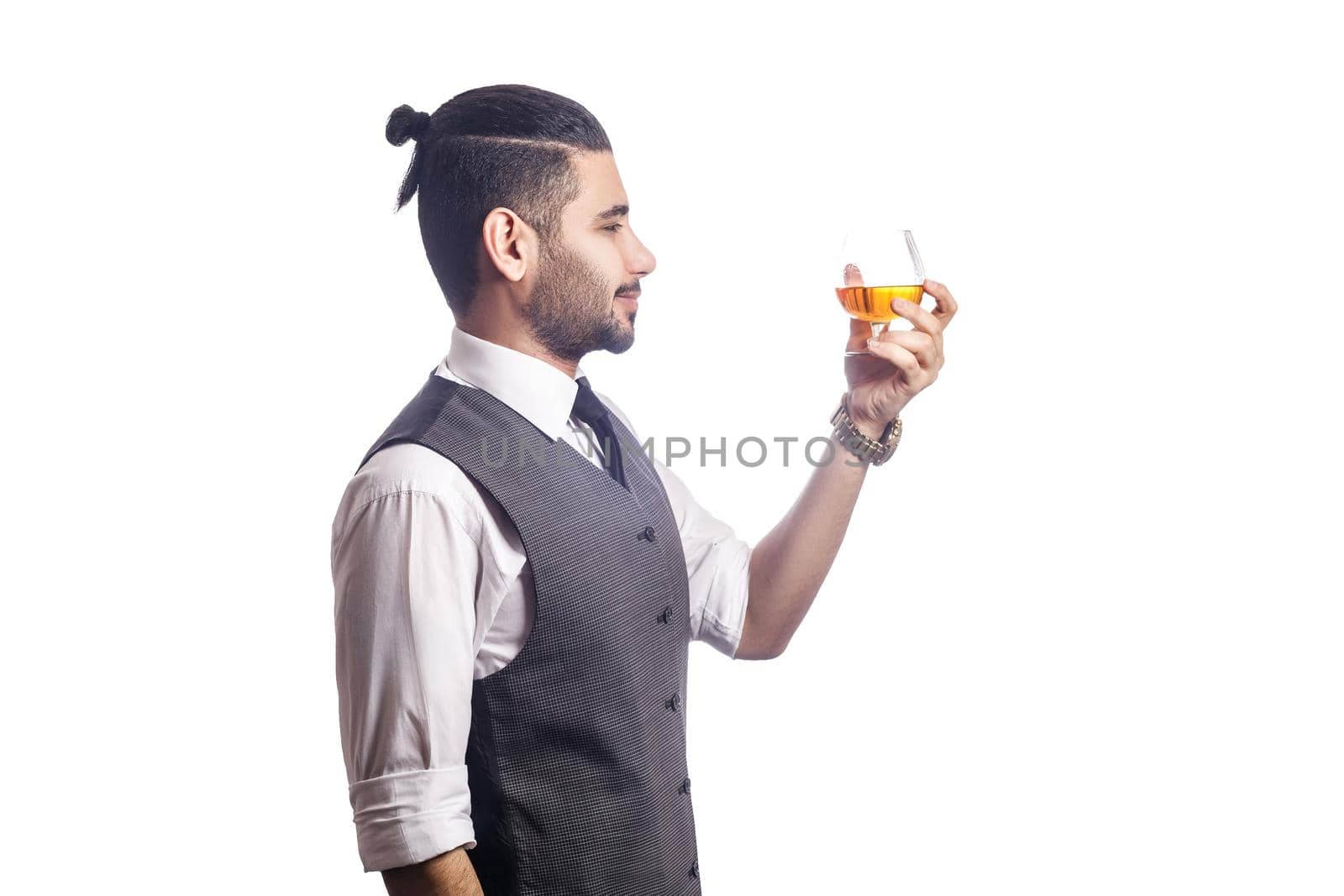 Handsome bearded businessman holding a glass of whiskey. side view. looking at glass and smiling, studio shot, isolated on white background.