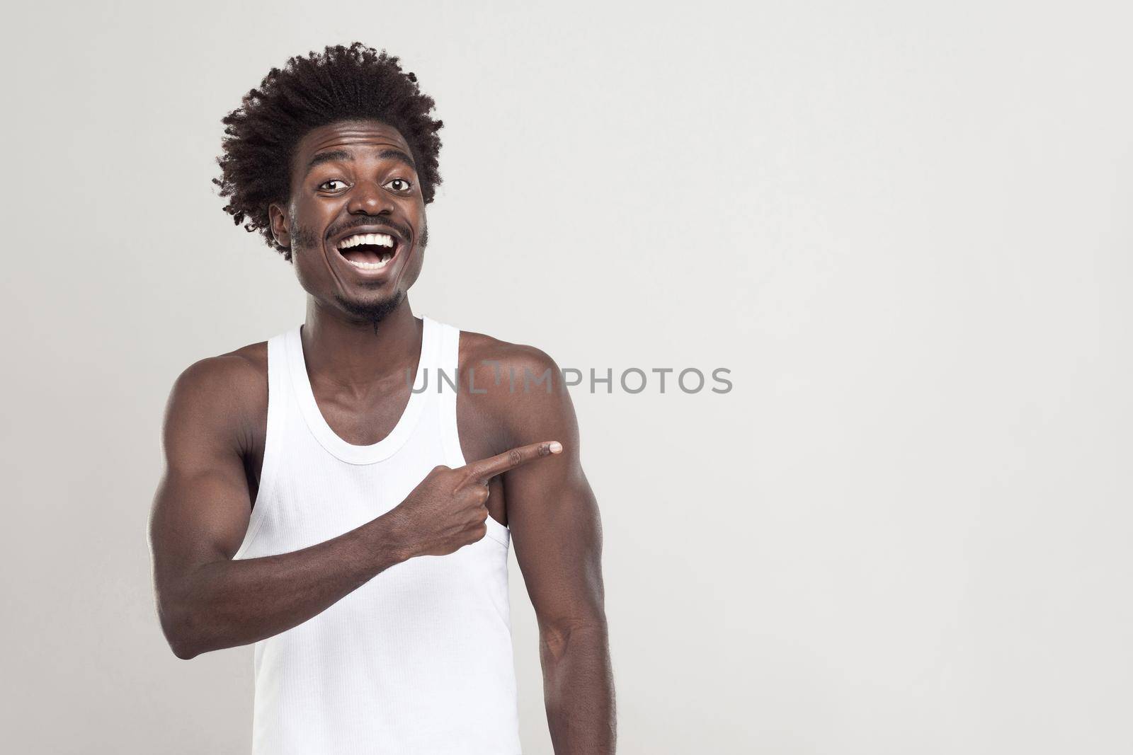 Man in white t-shirt showing finger at copy space. Studio shot. Gray background
