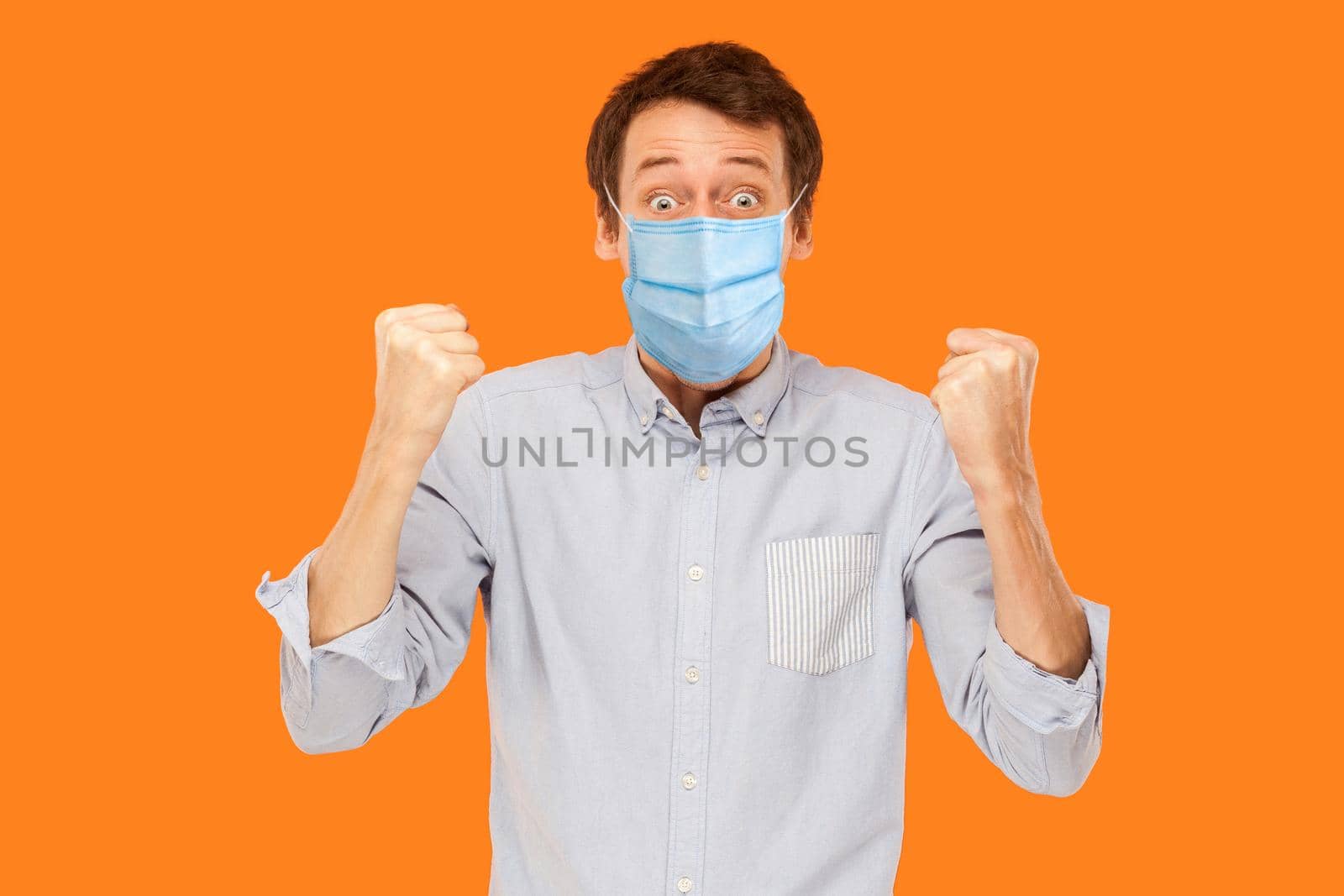 Yes. Portrait of surprised young worker man with surgical medical mask standing and celebrating his victory and looking at camera. indoor studio shot isolated on orange background.