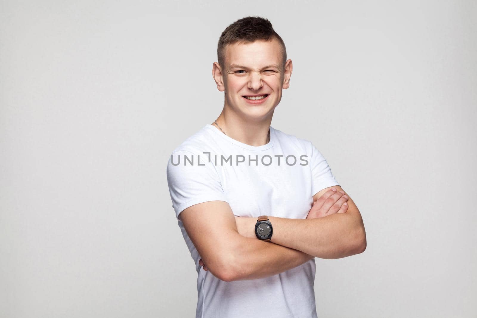 Boy crossed hands toothy smile and wink at camera. Studio shot