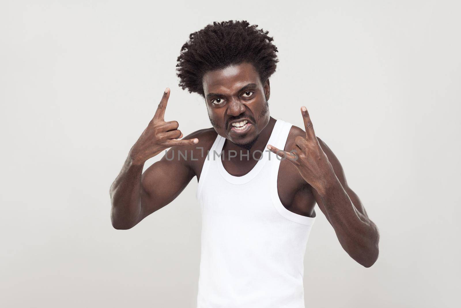 Aggressive afro man showing rock sign, looking at camera. Studio shot. Gray background