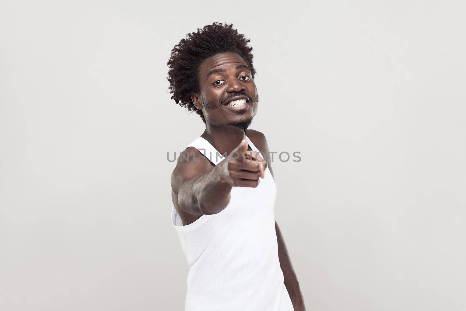 Hey you! Man in white t-shirt showing finger at camera. Studio shot. Gray background