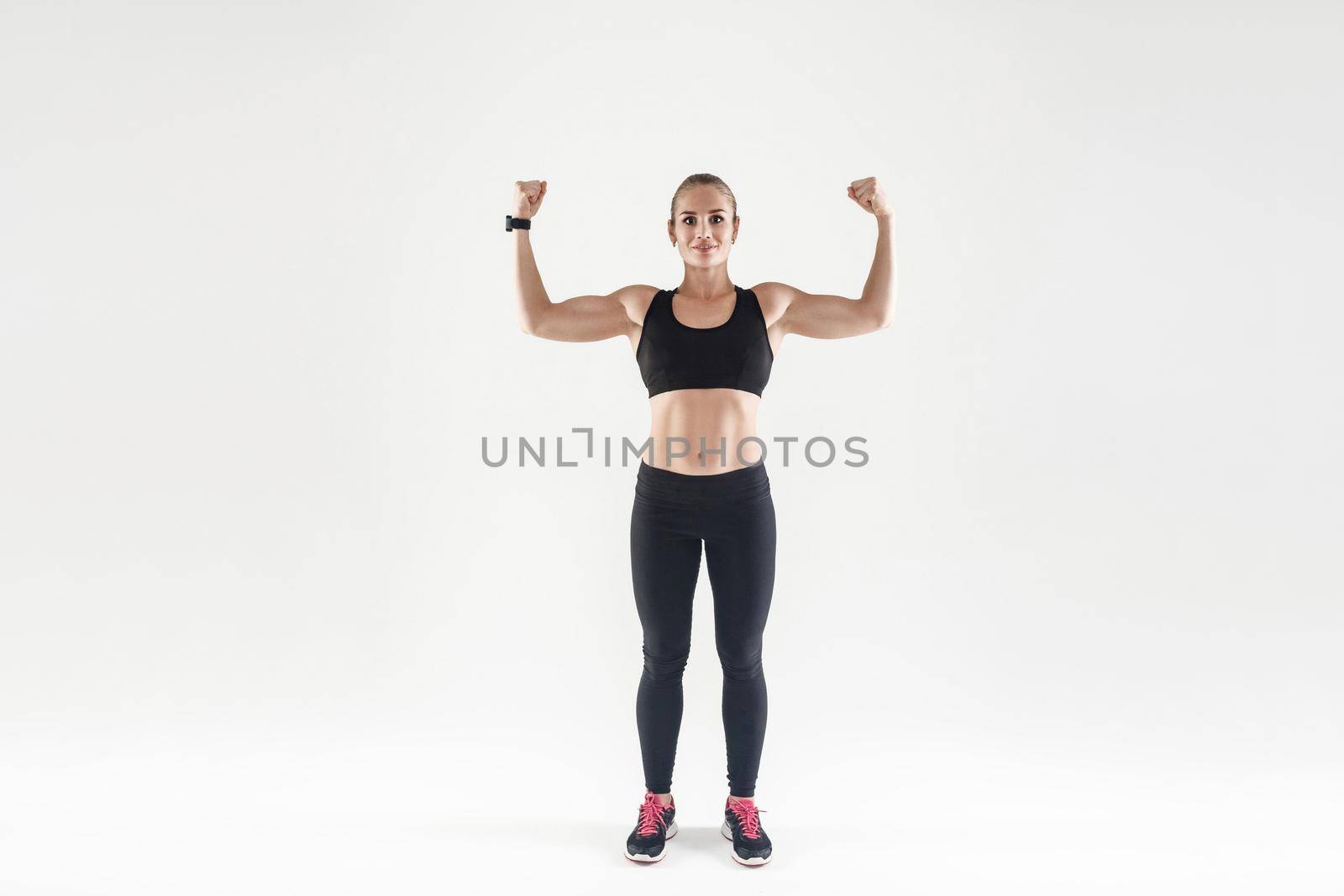 Bodybuilding concept. Powerful, attractive muscular girl engaged fitness. Woman showing her biceps at camera and smiling. Studio shot, gray background