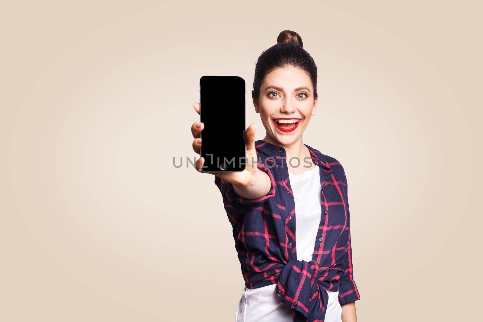 Young beautiful woman in casual style holding phone looking at camera and showing phone display. studio shot on beige background.