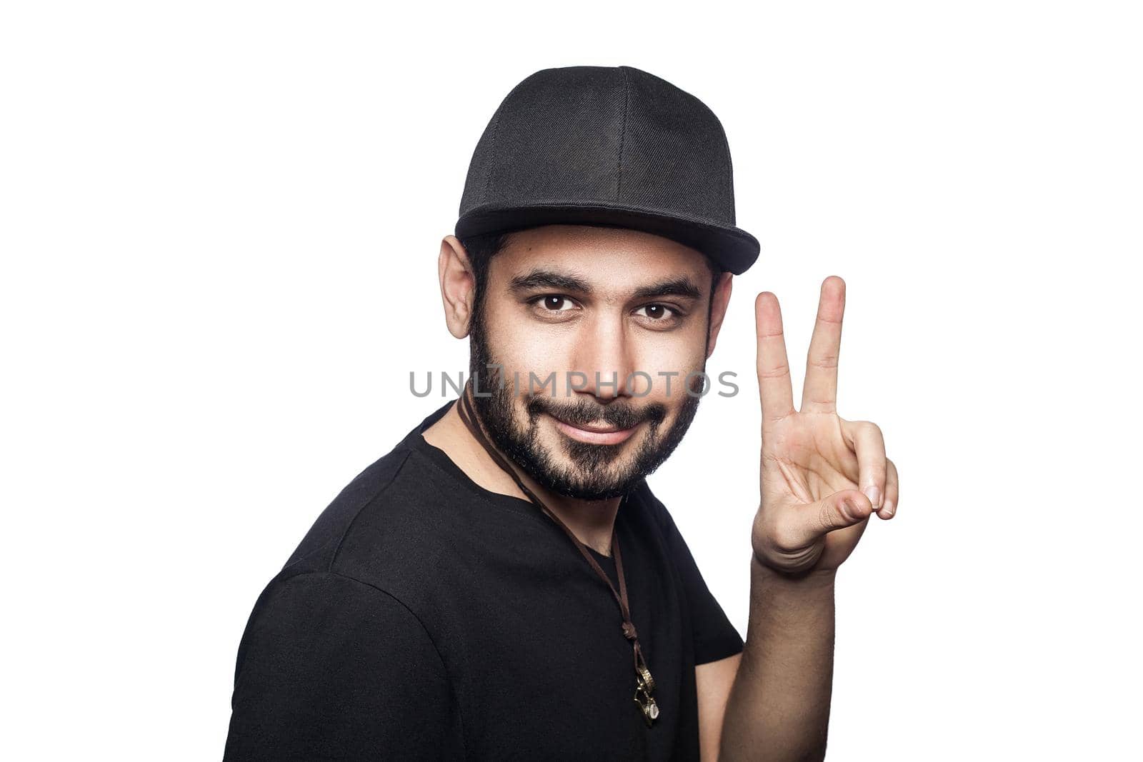 Portrait of young man with black t-shirt and cap looking at camera with victory sign. studio shot, isolated on white background.