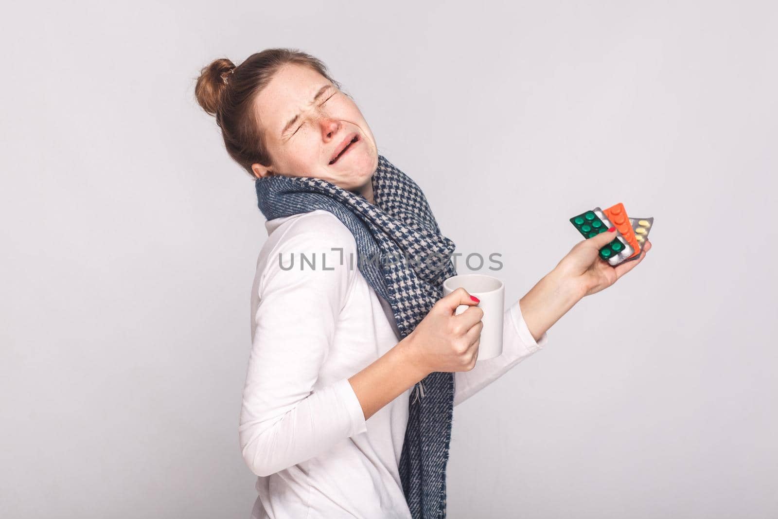 Woman cry because she was sick. Holding cup with tea, many pills and antibiotics. Studio shot, isolated on gray background