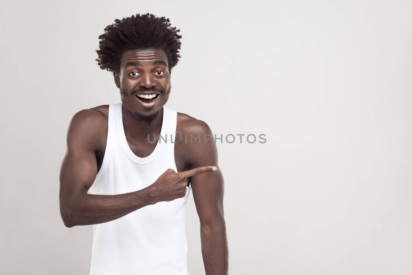 Amazement afro man, pointing finger at copy space. Studio shot. Gray background