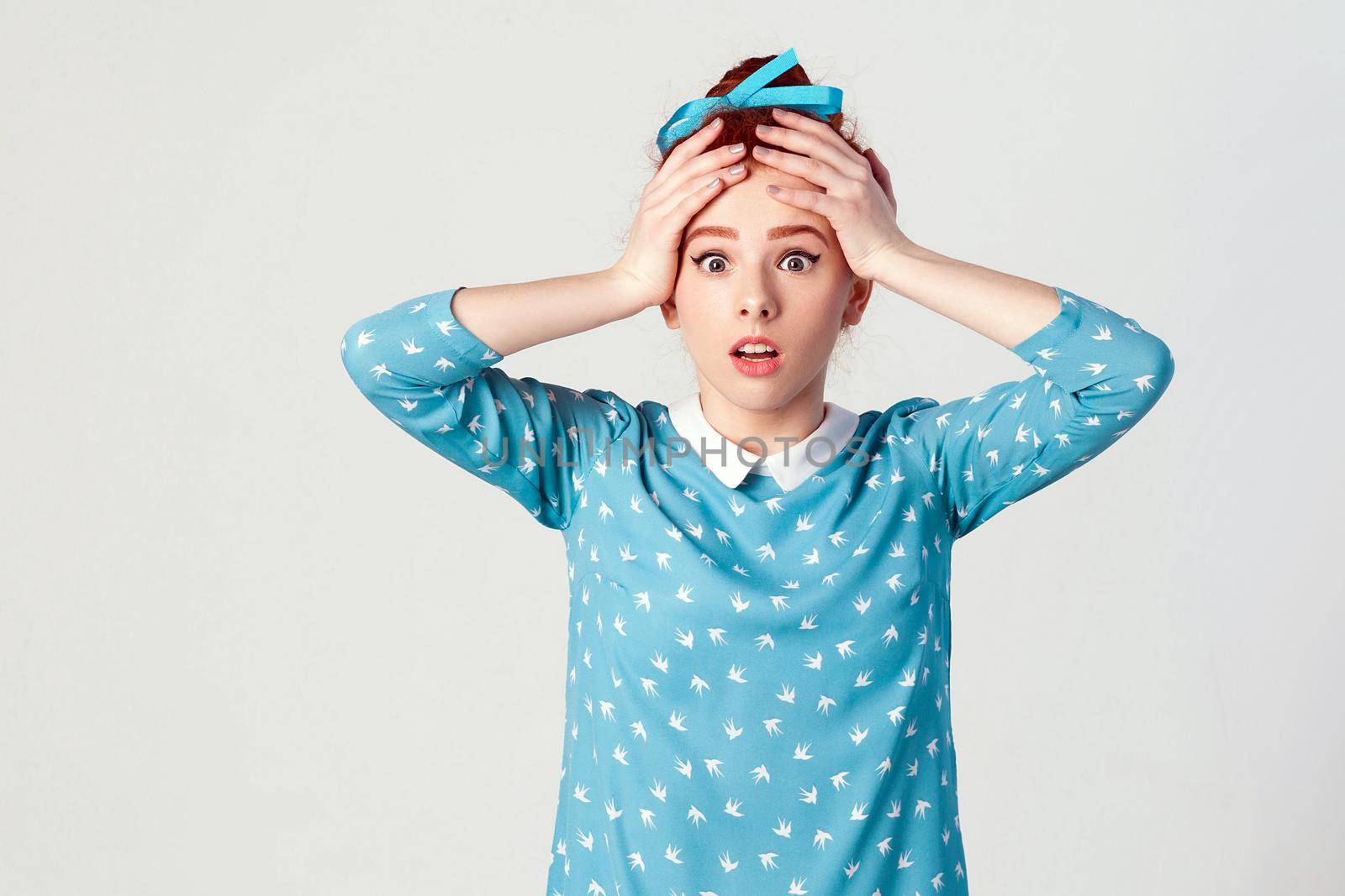 Human face expressions and emotions. Redhead girl looking desperate and panic, holding hands on her head, screaming with mouth wide open. Isolated studio shot on gray background