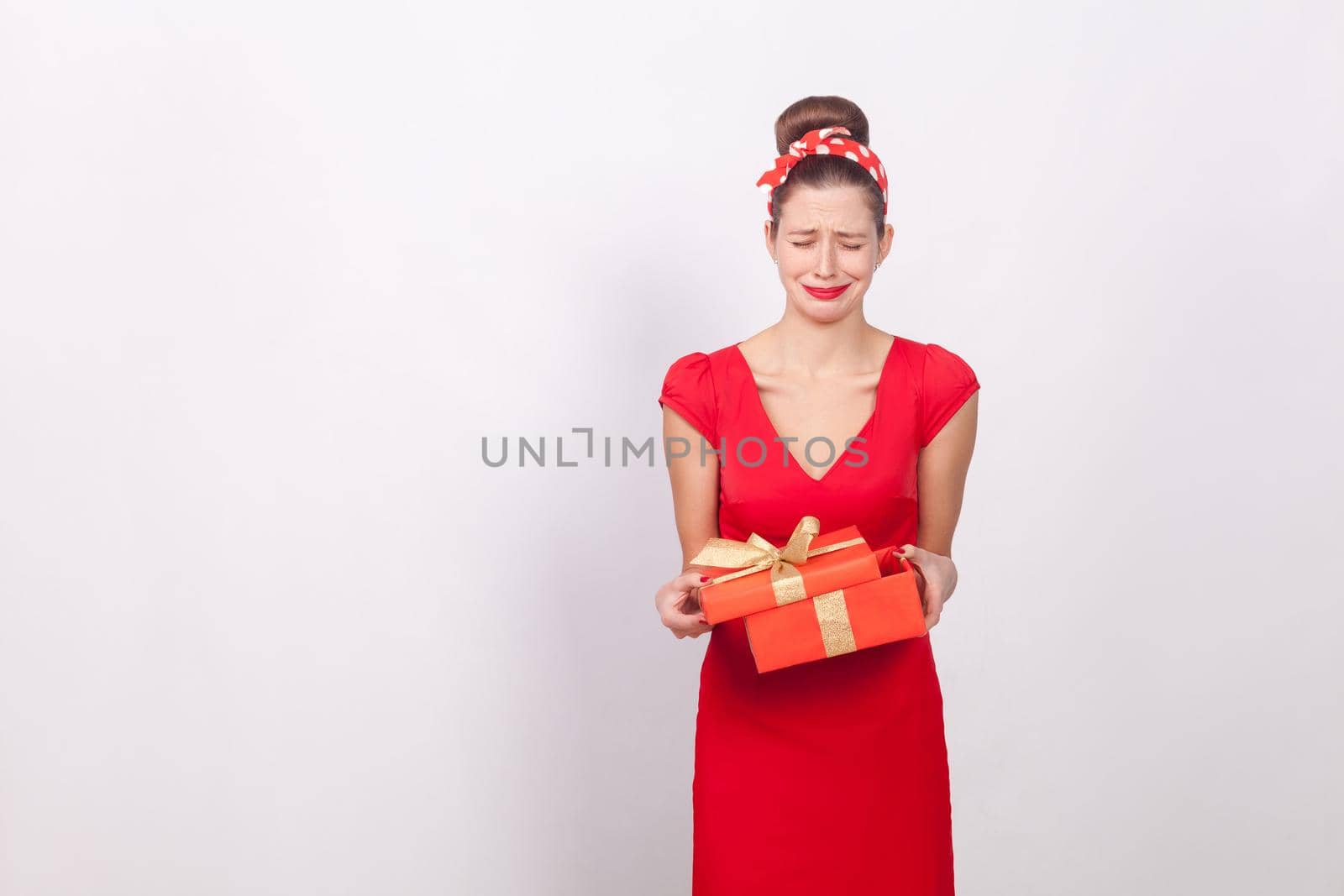 Disappointment. Woman holding red box and cry. Bad gift. Indoor, studio shot, isolated on gray background