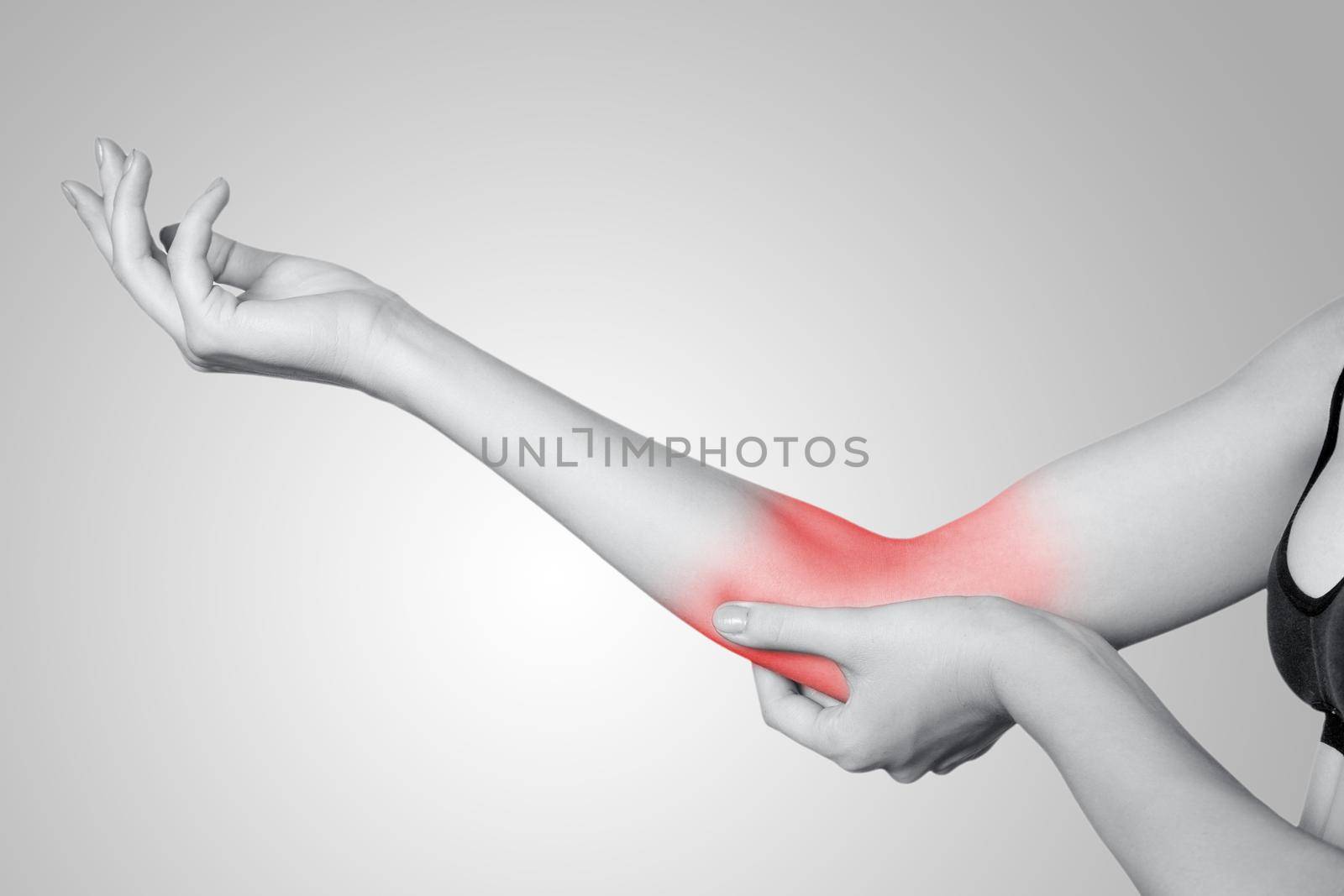 Closeup view of a young woman with elbow pain on gray background. Black and white photo with red dot.