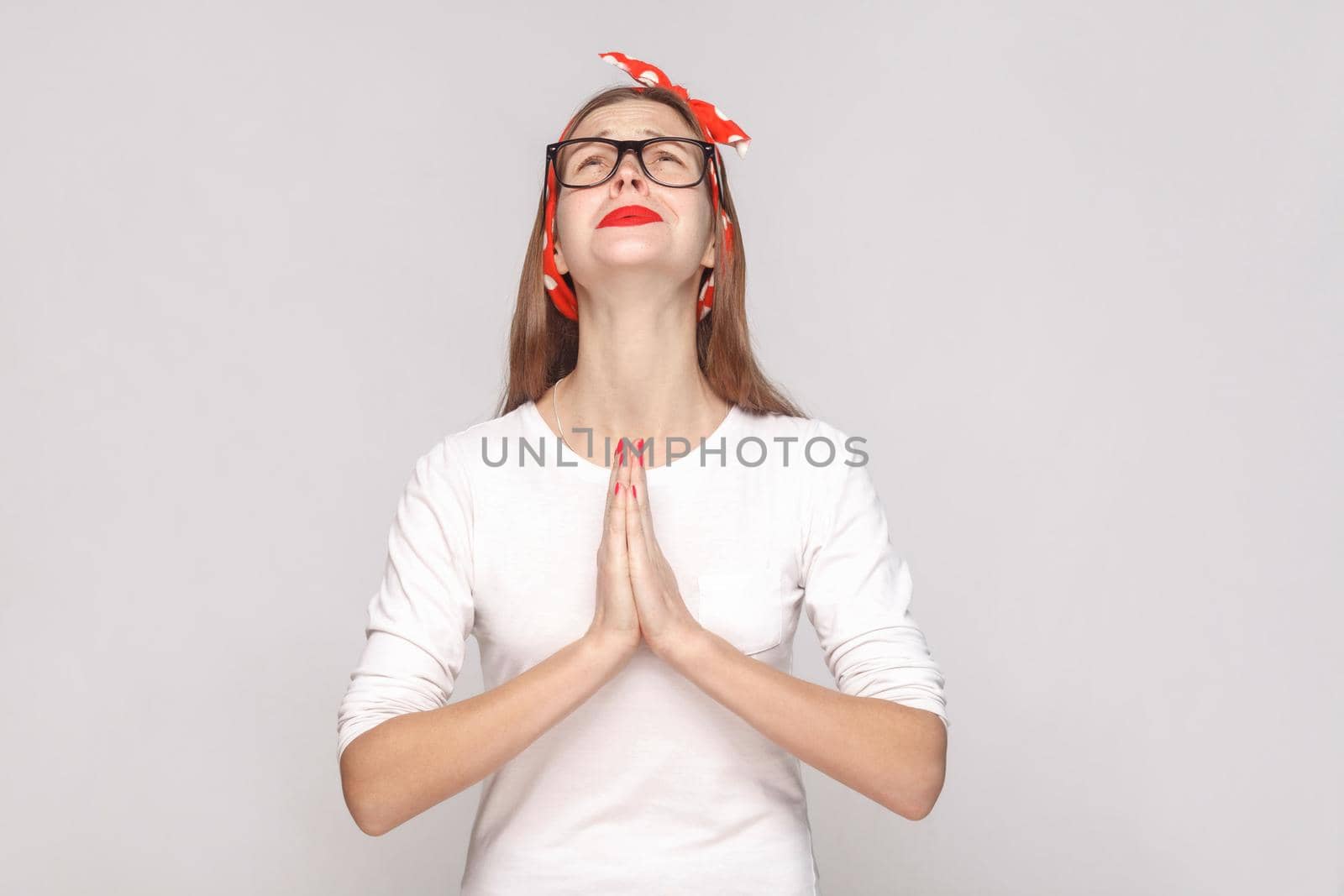 Oh my God please help me. portrait of beautiful emotional young woman in white t-shirt with freckles, black glasses, red lips and head band. indoor studio shot, isolated on light gray background.