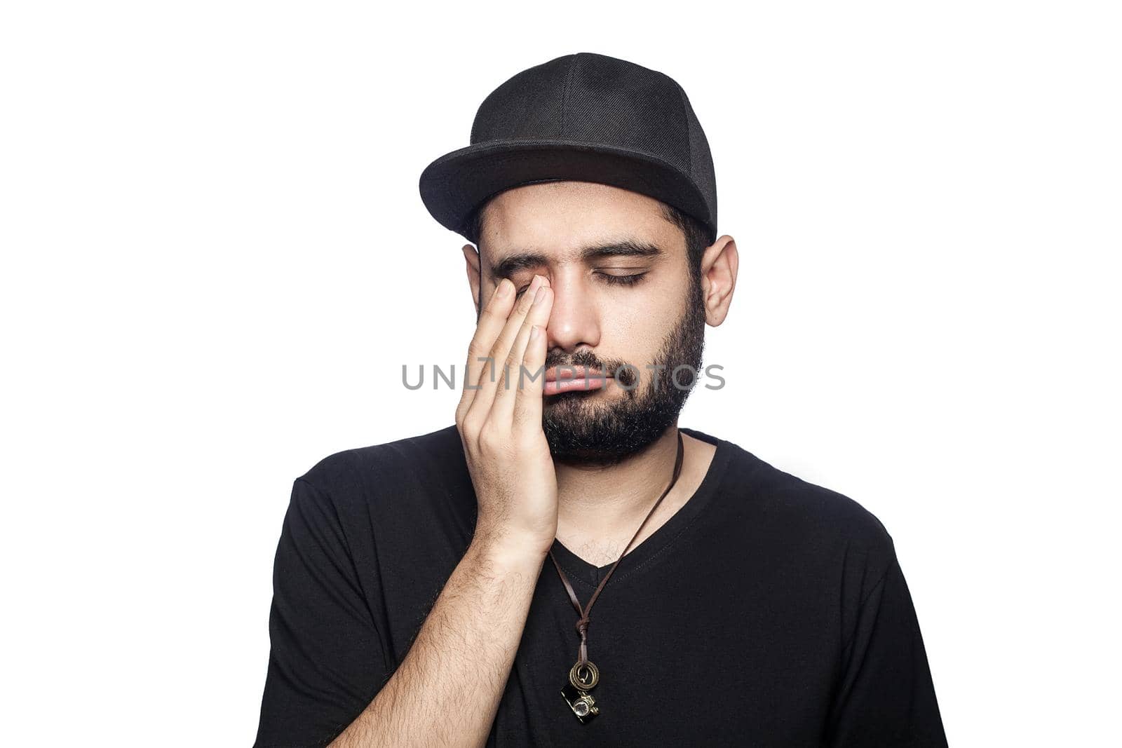 Portrait of young unhappy sad man with black t-shirt and cap looking at camera crying closed eyes. studio shot, isolated on white background.