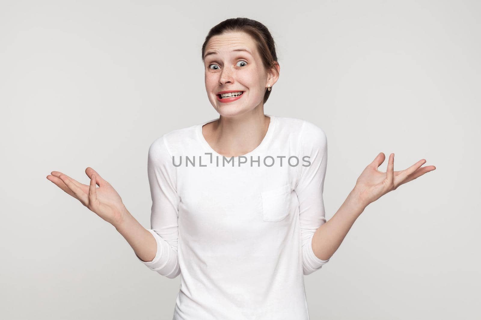 Who knows? Funny woman looking at camera with shocked face. Studio shot,isolated on gray background.