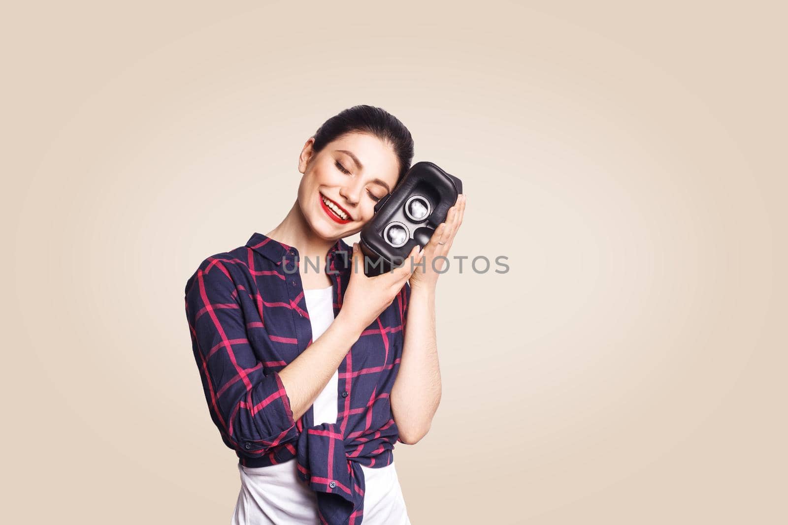 Young beautiful woman in casual style with virtual reality headset on beige background. studio shot. .