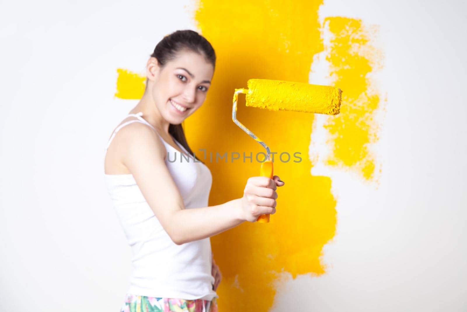 Beautiful young caucasian model in coloured shorts and white shirt and posing holding outrigger in her hands, painting the wall and looking at camera. Studio shot.